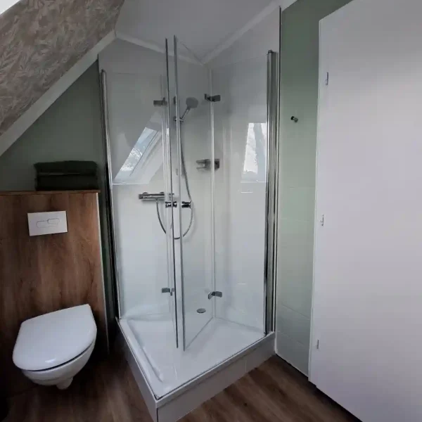 Ferienwohnung Hahn-Lehmden: Modernes Badezimmer mit Glasdusche und Holzoptik im hellen Dachgeschoss.