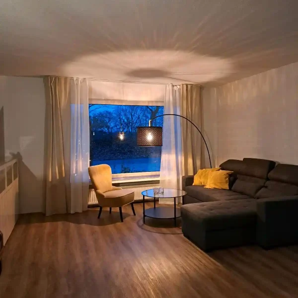 Ferienhaus Norddeutschland: Gemütliches Wohnzimmer-Ambiente mit Designer-Lampe und Blick in den Garten bei Dämmerung.