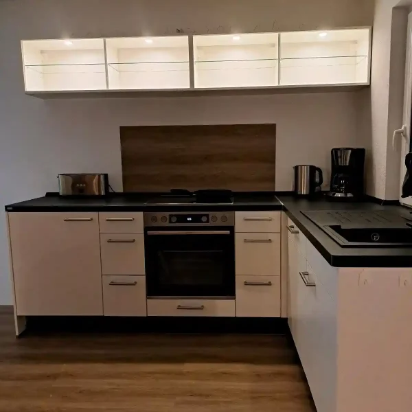 Hahn im Grün: Moderne Einbauküche mit Vollausstattung und beleuchteten Vitrinen für Selbstversorger im Ammerland.