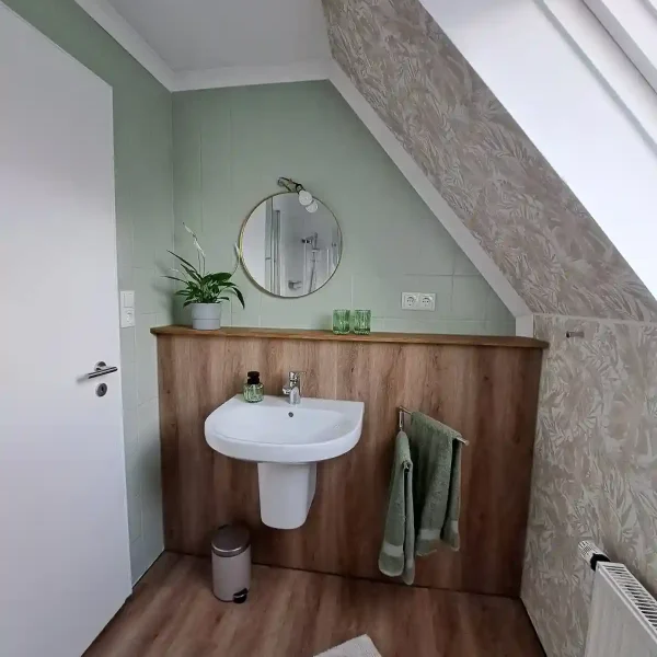 Unterkunft Ammerland: Design-Waschplatz mit rundem Spiegel und grünen Akzenten in der Ferienwohnung oben