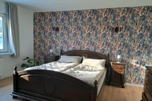 Monteurzimmer Hahn-Lehmden: Schlafzimmer mit dunklem Massivholzbett und floraler Vintage-Tapete mieten.