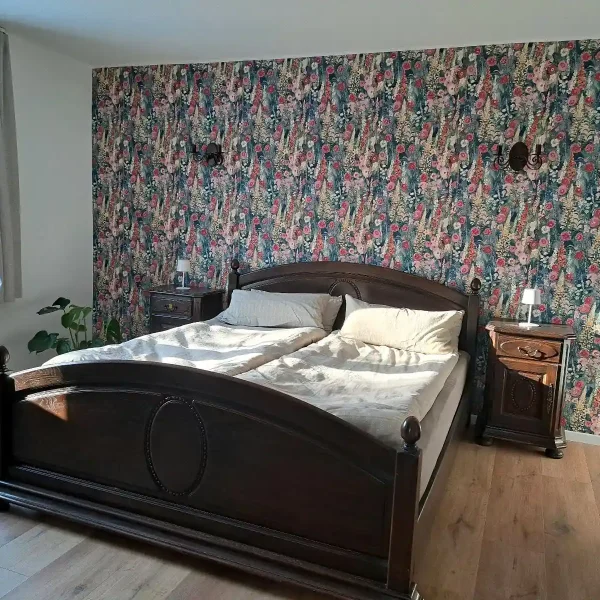 Ferienwohnung Ammerland: Schlafzimmer mit prunkvollem dunklem Doppelbett und floraler Vintage-Tapete.