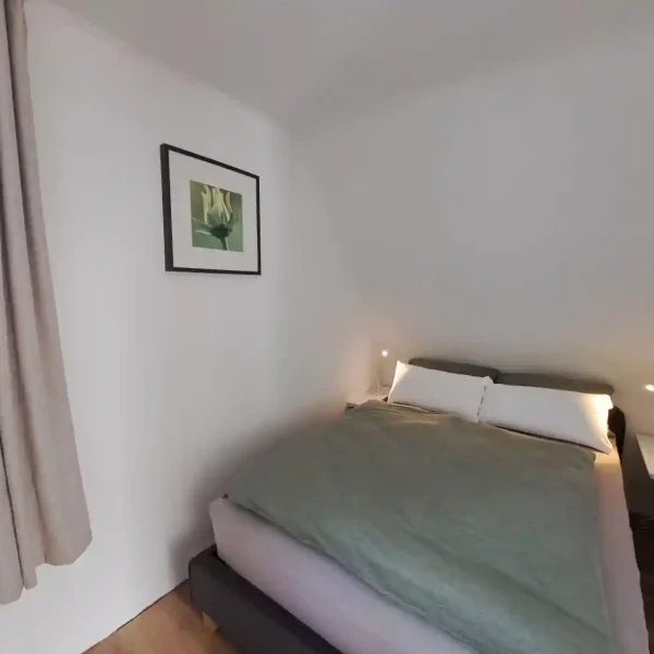 Ferienhaus Ammerland: Gemütliches Schlafzimmer im Dachgeschoss mit Doppelbett und salbeigrüner Bettwäsche.