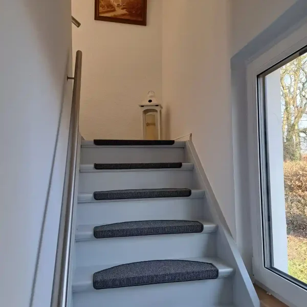 Ferienwohnung Rastede: Heller Treppenaufgang zum Obergeschoss mit maritimer Dekoration und viel Licht.