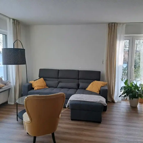 Ferienwohnung Ammerland: Helle Leseecke mit gelbem Sessel und großem Panoramafenster in den Garten.